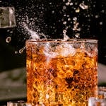 Close-up shot of a scotch glass with ice cubes splashing in a dynamic bar scene.
