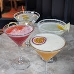 Four vibrant cocktails in martini glasses on a marble surface.