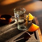 Two tequila shots with lemon slices and salt on a rustic tray in warm light.